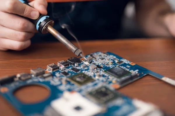 Een man met een soldeerbout reparaties computerapparatuur. — Stockfoto