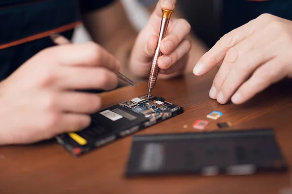 Un hombre está reparando un teléfono móvil. En el marco, sus manos y detalles del dispositivo . — Foto de Stock