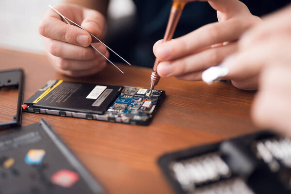 A man is repairing a mobile phone. In the frame, his hands and details of the device.