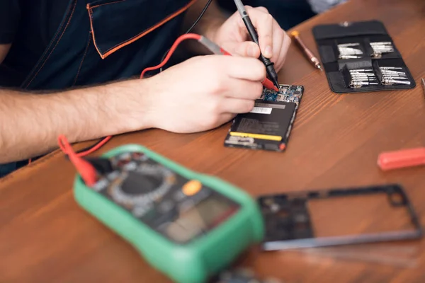 A man is repairing a mobile phone. In the frame, his hands and details of the device.