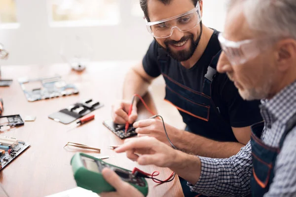 Äldre och unga män reparera en mobiltelefon tillsammans. — Stockfoto