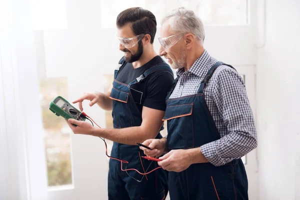 Ouderen en jonge mannen onderzoeken samen een digitale multimeter. — Stockfoto