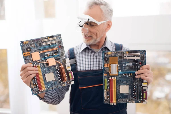 An elderly computer repair specialist is posing for a camera with a motherboard.