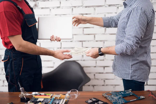 An elderly man gives money to a computer repairman. He came to the workshop of electrical engineering.