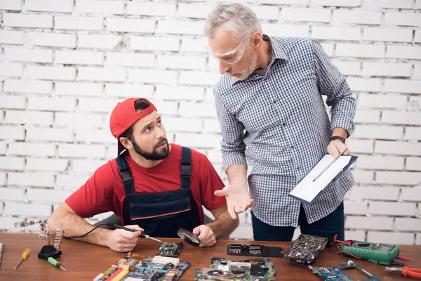 De manager van de computer reparatie winkel is in gesprek met een meester die solder deel van de computer. — Stockfoto