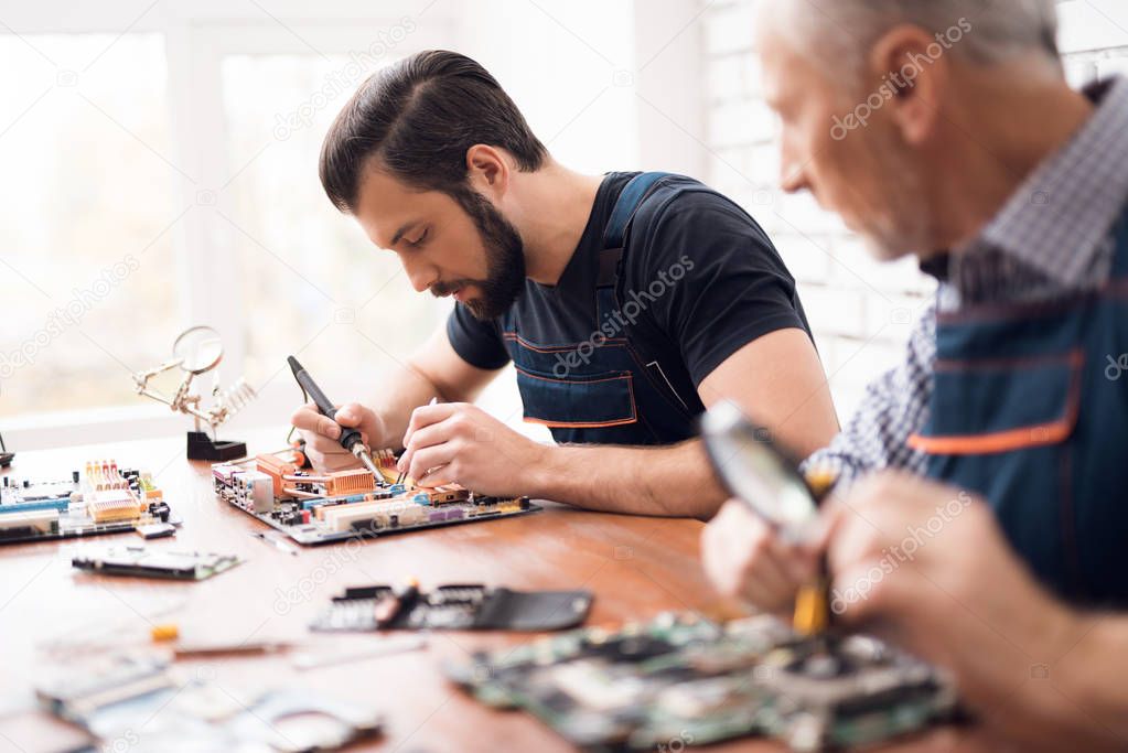 Adult and young men repair parts from the computer together.