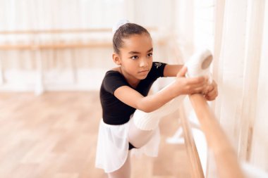 Kız bacaklarını bale barr yakınındaki bir streç eğitiyor.