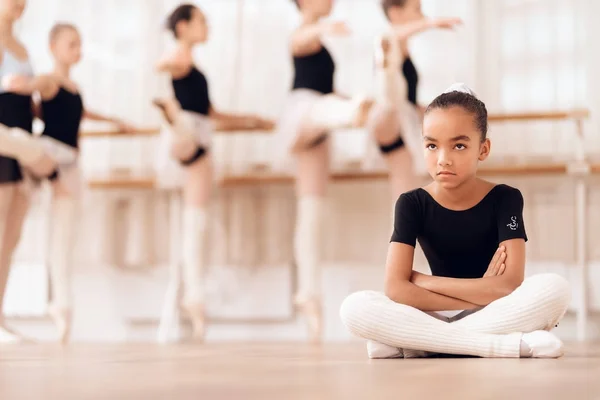 De jonge ballerina zit op de vloer tijdens het bijwonen van een balletschool. — Stockfoto