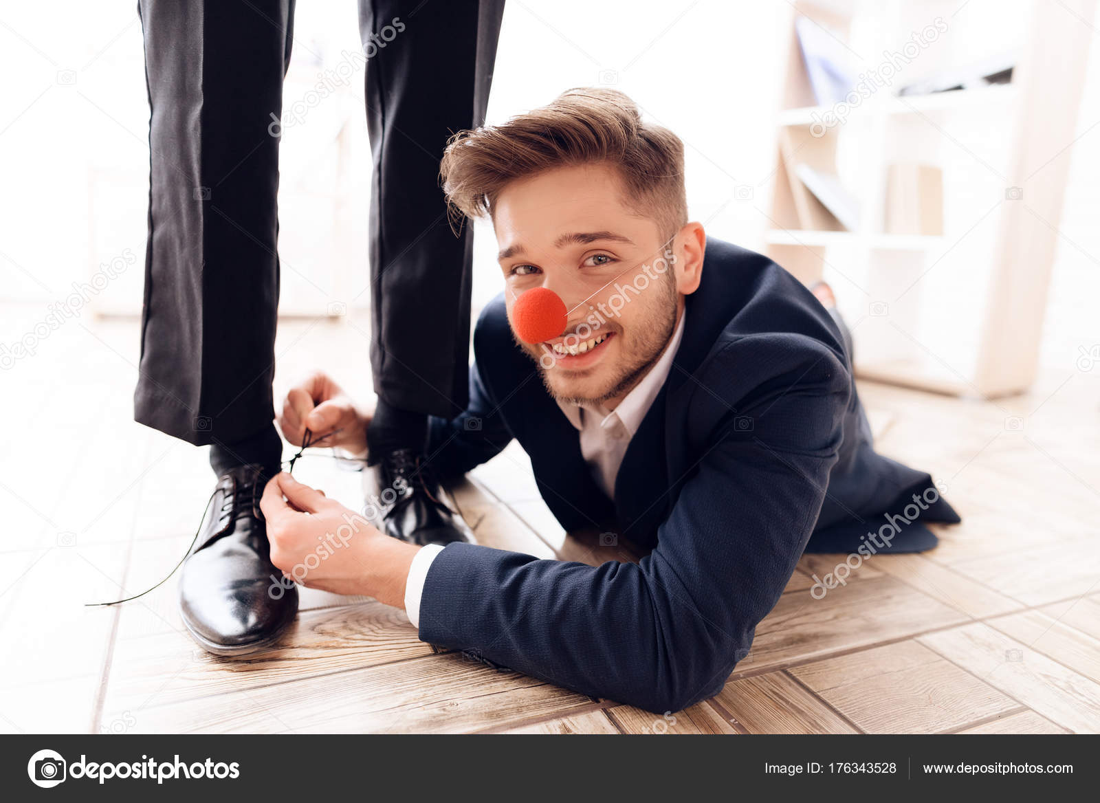 A man with a clown's nose under the table to tie laces to his business