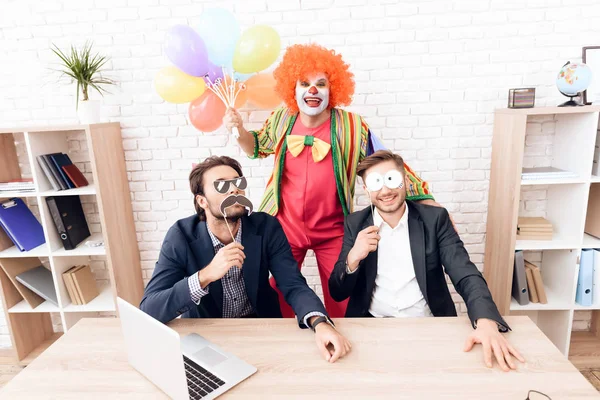 Muž v obleku klauna stojí vedle dalších mužů v jasné obchodní kancelář Fools' den. — Stock fotografie