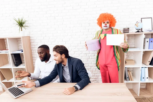 Człowiek w garniturze clown stoi obok innych mężczyzn w biurze firmy jasne na Fools' Day. — Zdjęcie stockowe