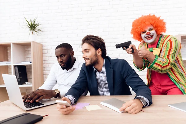Muž v obleku klaun je míření zbraní na podnikatele v světlé kanceláři. — Stock fotografie