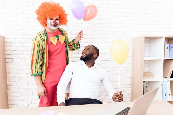 Człowiek w garniturze clown stoi obok czarny człowiek, który siedzi przy biurku. — Zdjęcie stockowe