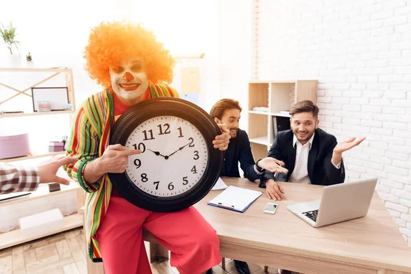 Un uomo vestito da clown sta accanto a uomini in giacca e cravatta, che siedono alla scrivania . — Foto Stock
