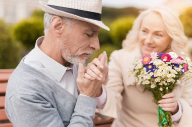 İki emekliler sokakta bir bankta oturuyor. Yaşlı bir adam yavaşça bir kadının elini öper