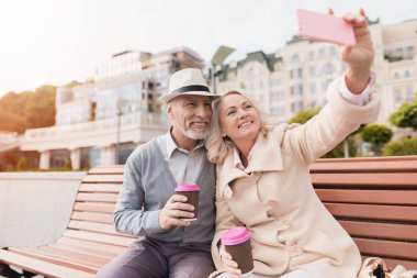 İki emekliler ile bir bardak kahve ellerinde bir bankta oturuyor. Bir kadının Smartphone'da selfies yapıyorlar