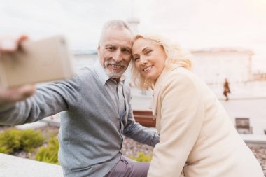 Bir yaşlı çift bir Çiçeklik kenarında oturuyor. Smartphone selfie yapıyorlar
