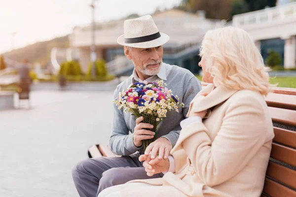 2 つの年金受給者は、路地でベンチに座っています。初老の男性は、女性の花を与える — ストック写真