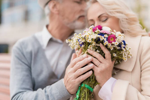 Dos pensionistas están sentados en un banco en el callejón. El anciano le dio flores a la mujer. Él sostiene su mano — Foto de Stock