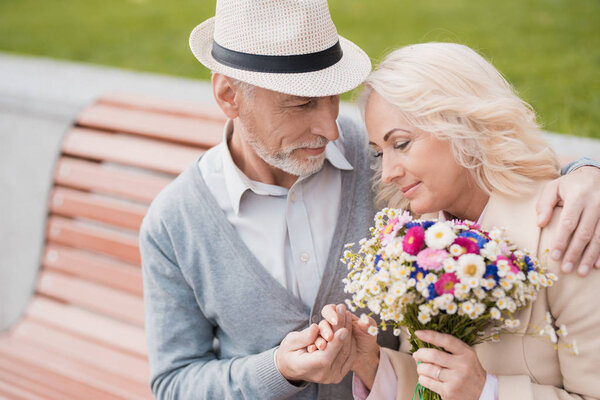 Two pensioners are sitting on a bench in the alley. An elderly man gently holds her hand