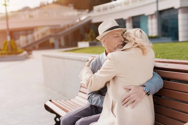 Dois pensionistas estão sentados em um banco na praça. Eles gentilmente abraçam sentado no banco — Fotografia de Stock