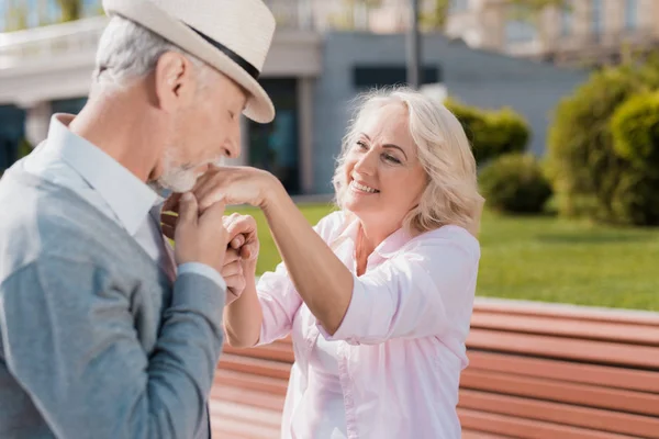 Una pareja de ancianos está caminando en la plaza. El hombre besa la mano de la mujer. Ella sonríe — Foto de Stock