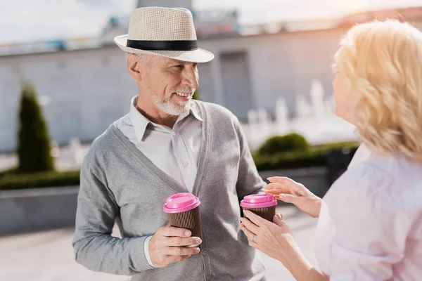 Una pareja de ancianos está caminando en la plaza. Beben café y se divierten — Foto de Stock