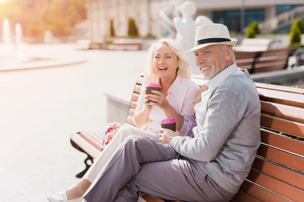 Una pareja de ancianos está caminando en la plaza. Beben café y se divierten — Foto de Stock