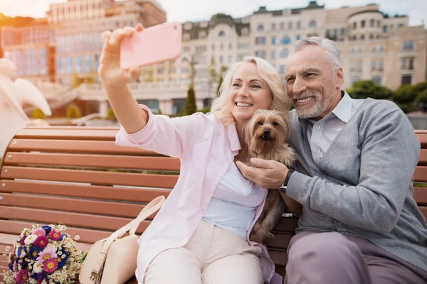 Yaşlı bir çift ile küçük köpeği meydanda yürüyor. Bir köpek ile bir selfie yapıyorlar