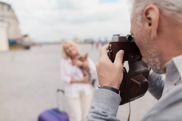 An elderly couple is walking. A woman poses with a dog in her arms, a man takes pictures of her on a film camera — Stock Photo, Image