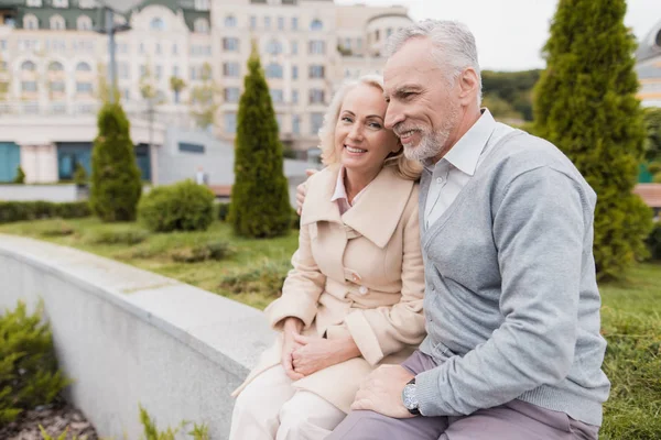 Una pareja de ancianos está sentada en el borde de un macizo de flores. Se sonríen. —  Fotos de Stock