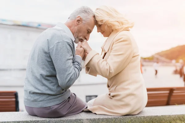 Una pareja de ancianos está sentada en el borde de un macizo de flores. Se toman de la mano . — Foto de Stock