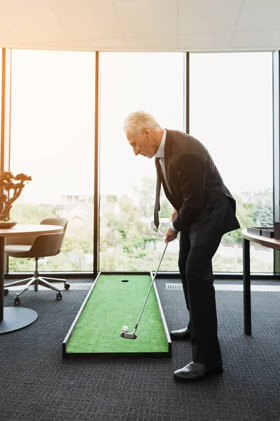 En man i en strikt kostym spelar i ett kontor i en mini-golfbana — Stockfoto