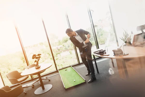 Um homem em um terno de negócios estrito joga em um escritório em um mini-golf — Fotografia de Stock