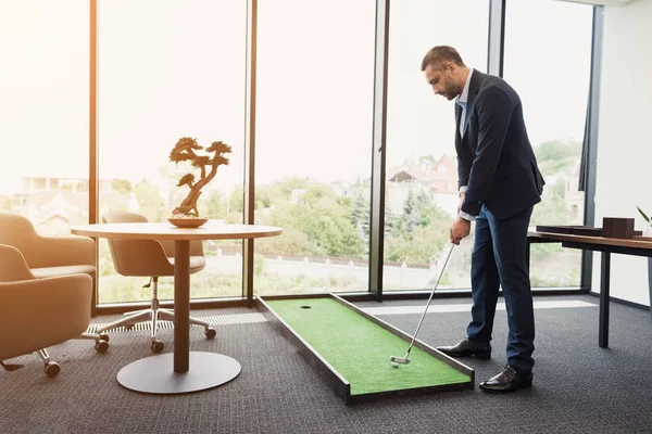 Un hombre con un estricto traje de negocios juega en una oficina en un mini-golf — Foto de Stock