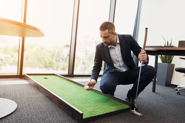 Um homem em um terno de negócios estrito joga em um escritório em um mini-golf — Fotografia de Stock