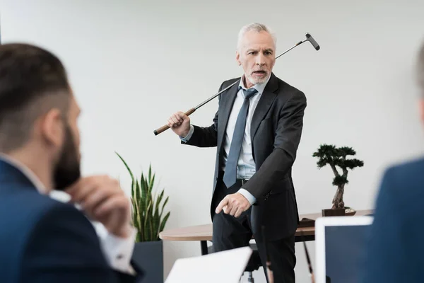 Deux employés sont venus au bureau du directeur pendant qu'il jouait au golf. Il leur crie dessus. . — Photo