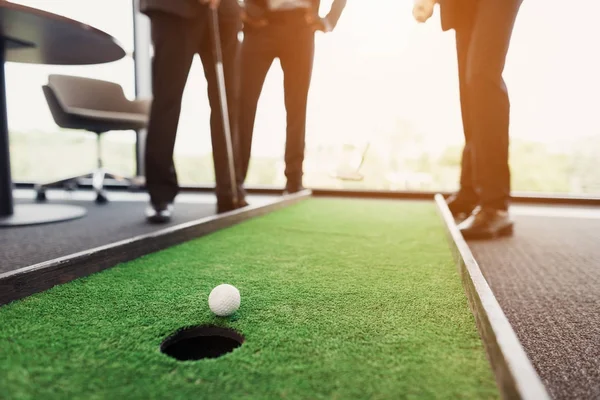 De cerca. Los hombres juegan en una oficina en un mini golf. Uno de ellos tiene un palo de golf en sus manos. — Foto de Stock