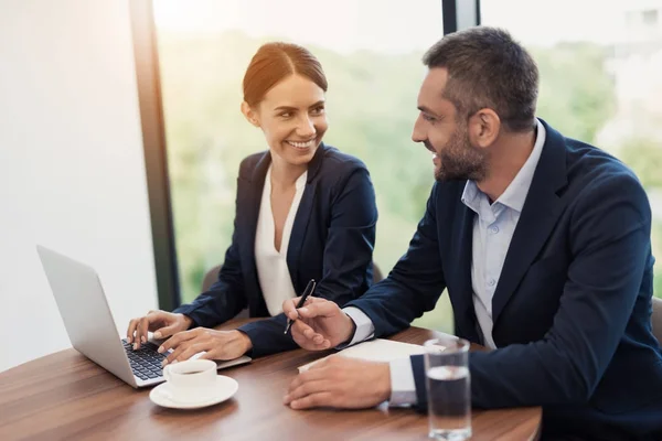 Um homem e uma mulher em trajes de negócios rigorosos estão discutindo algo enquanto se sentam em uma mesa com uma xícara de café — Fotografia de Stock