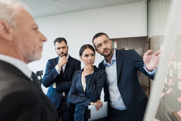 Tres empleados y su director están al lado del bastidor con el horario. Lo consideran cuidadosamente. —  Fotos de Stock