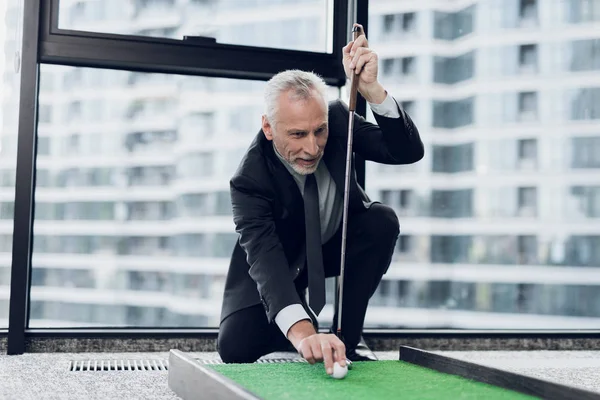 Un respetable anciano jugando un mini golf en la oficina. Pone la pelota antes del golpe — Foto de Stock