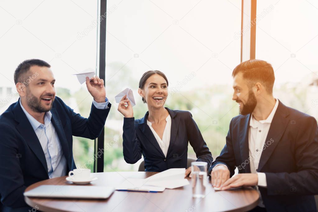 Three employees sit at the table at a meeting and are fooled. They launch paper airplanes and rejoice