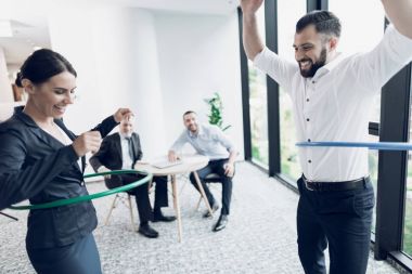 Eğlenceli ofis. Bir erkek ve bir kadın hula hoops twist. İki meslektaşlarının masaya otur ve onlara bakmak.