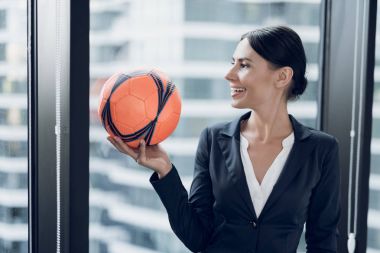 Sıkı iş takım elbiseli bir kadın turuncu bir futbol onun elinde tutar. O gülümsüyor