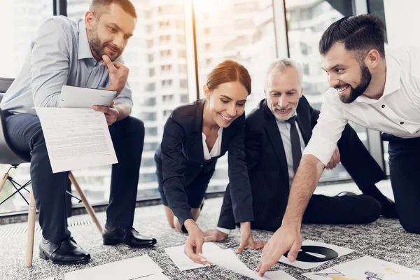 Eine ungewöhnliche Begegnung. Geschäftsleute sitzen auf dem Boden und betrachten Berichte, die auf dem Boden ausgelegt wurden.. — Stockfoto