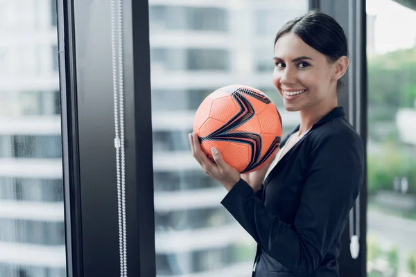 A woman in a strict business suit holds an orange football in her hands. She smiles — Stock Photo, Image