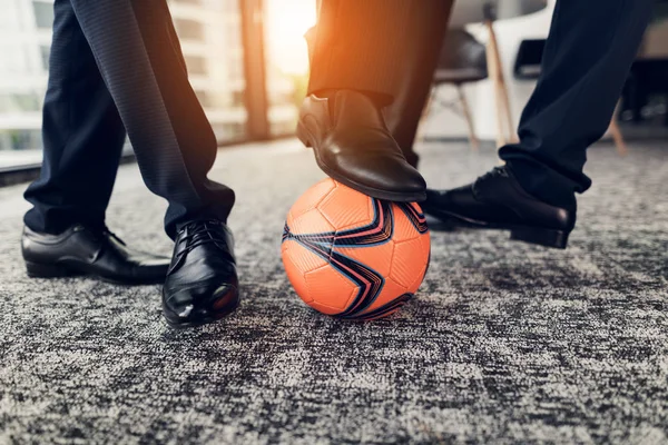 Close up. Three men in strict trousers and black shoes play an orange ball in football in the office — Stock Photo, Image