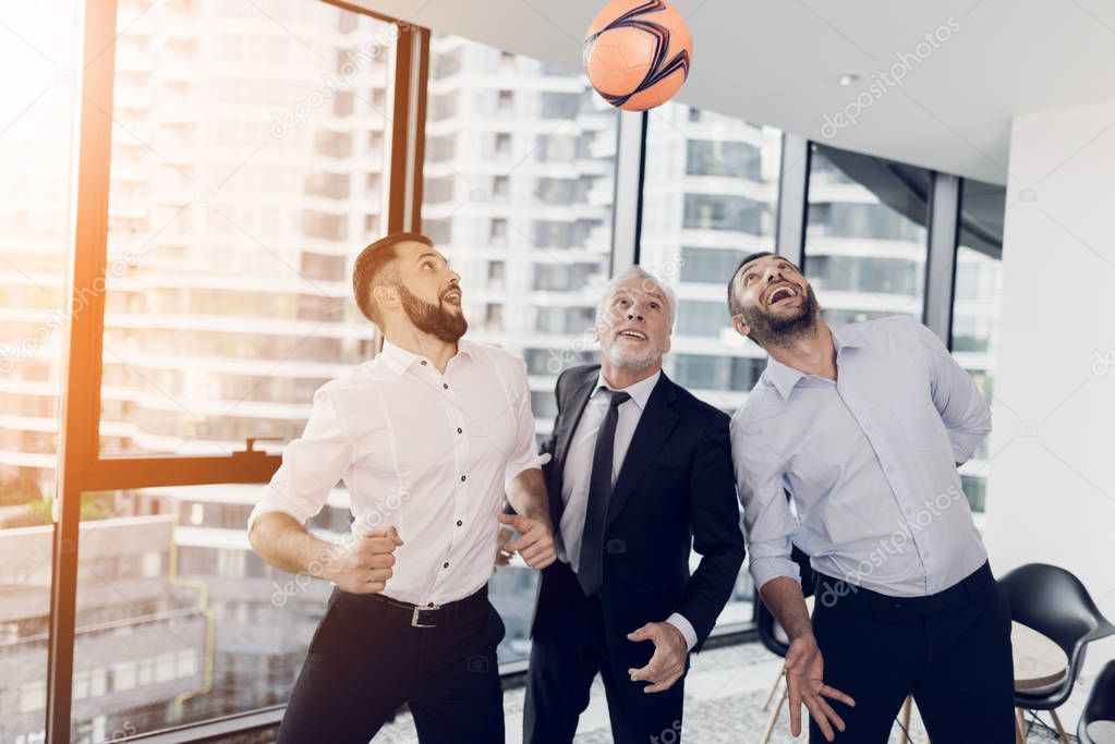 Three businessmen play football in the office with an orange soccer ball. They are having fun