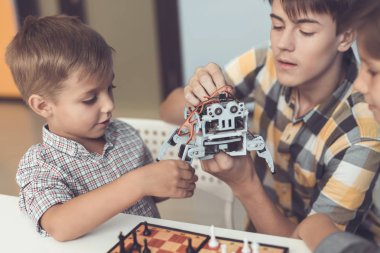 Adam gri bir robot bir masada oturan iki çocuk getirdi. Çocuk hevesle düşünüyorsanız