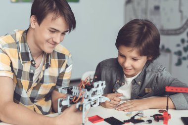 Adam ve oğlan masada oturuyor. Adam çocuğu nasıl robot ayarlandı gösterir